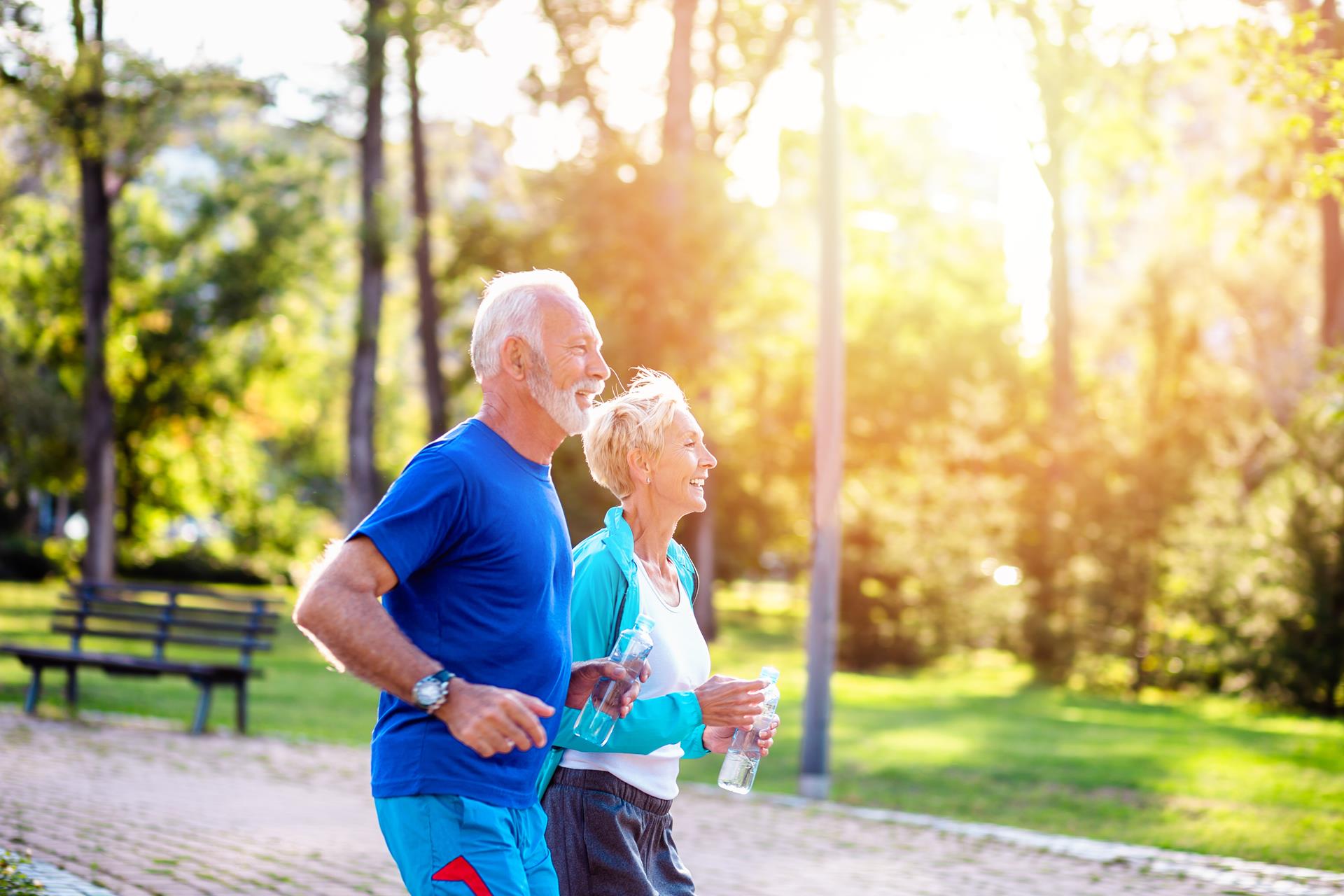 Happy senior couple jogging outdoors in park.